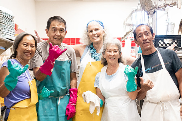 A group of people in aprons standing in a kitchen, preparing food and working together.