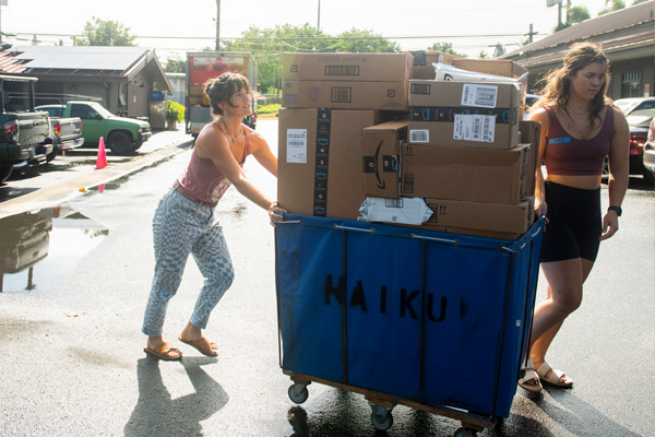 Two women pushing a cart loaded with boxes, demonstrating teamwork and collaboration.